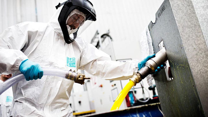 Worker wearing white safety overalls and helmet while manipulating hoses