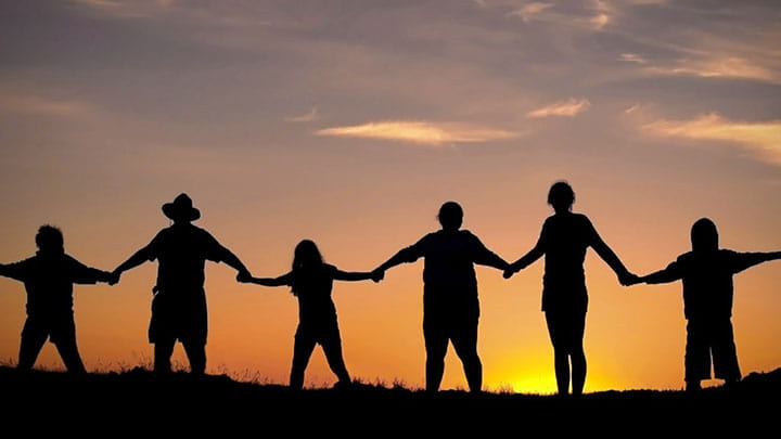 Six humans holding hands in front of sunset 