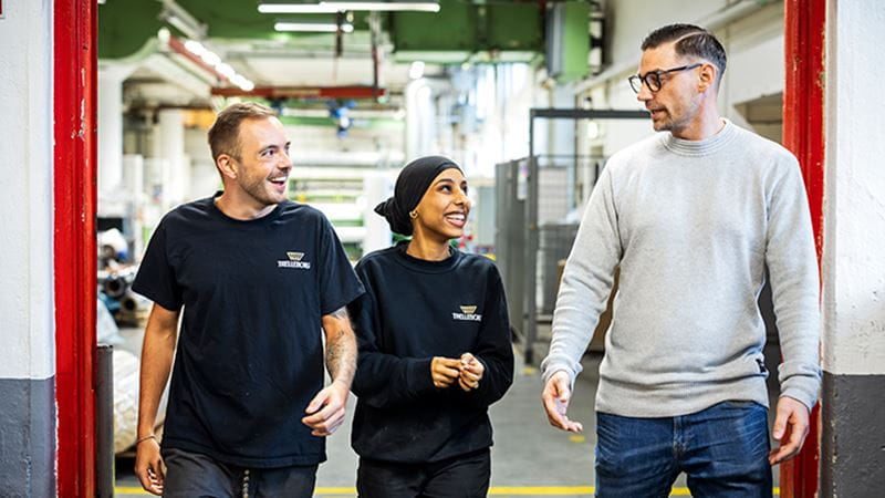 Tre glada personer engagerade i ett samtal går i en fabrik