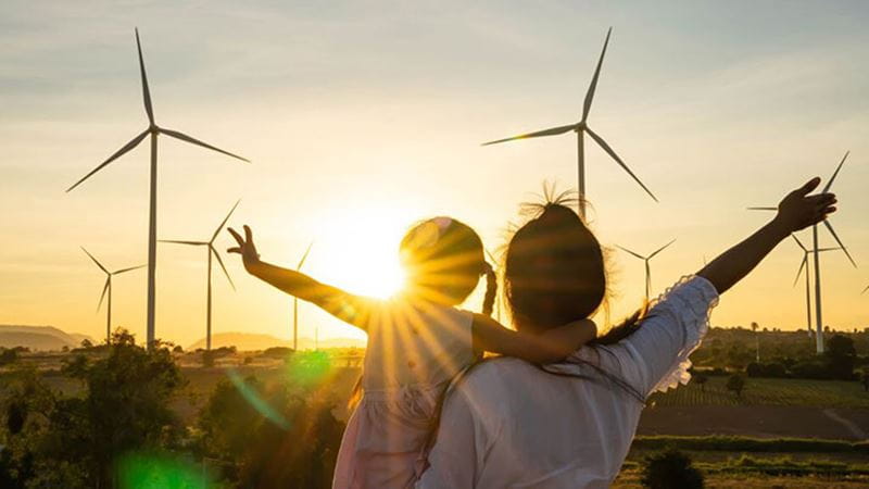 Vuxen och barn som blickar ut över vindkraftverk i solnedgången, som symboliserar förnybar energi och klimatarbete.
